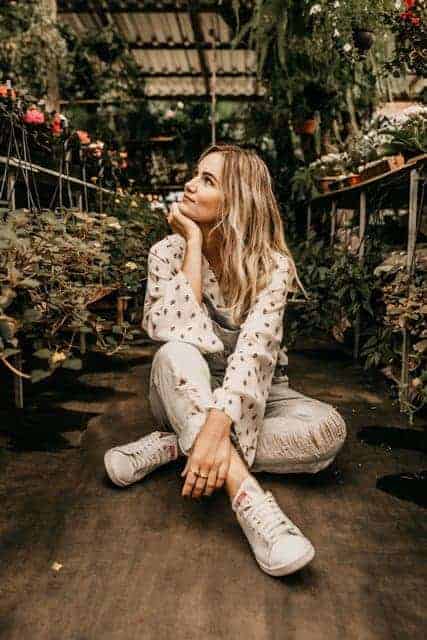 Blond girl sitting on ground in flower nursery gazing