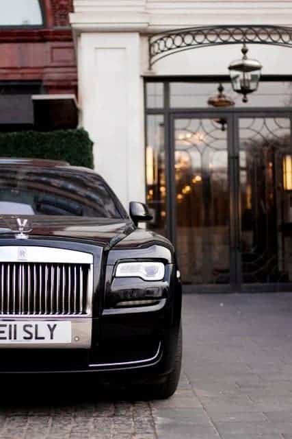 wealth Rolls Royce in front of mansion